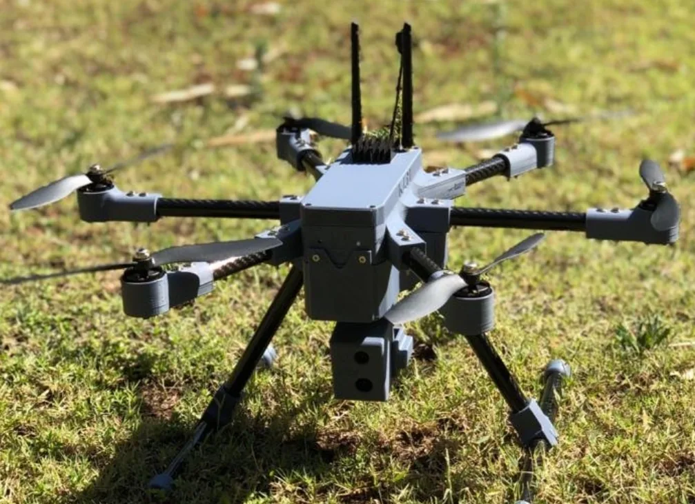 Close-up of the KLM Power Raptor V40 hexacopter drone with antennas and camera payload, sitting on grass